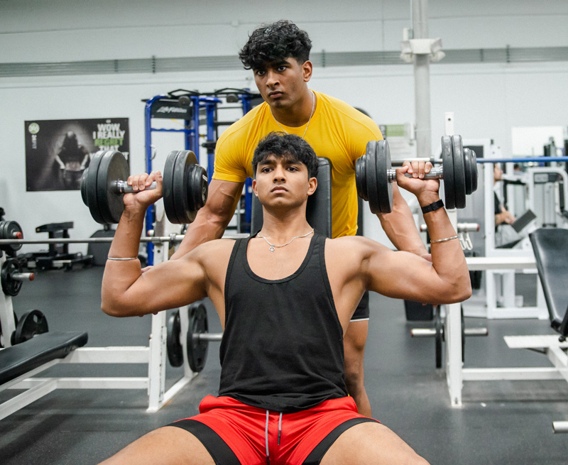 One of the coaches is assisting the other coach with biceps.
